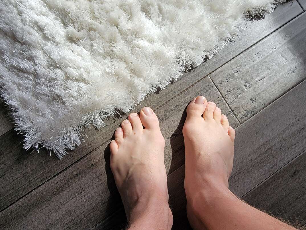 man s bare feet on the floor beside a white carpet