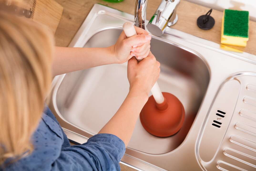 A female plumber fixing the kitchen sink with a plunger, Stock image