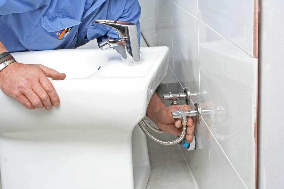 a plumber installs a bidet by connecting the water line to the fixture in the wall