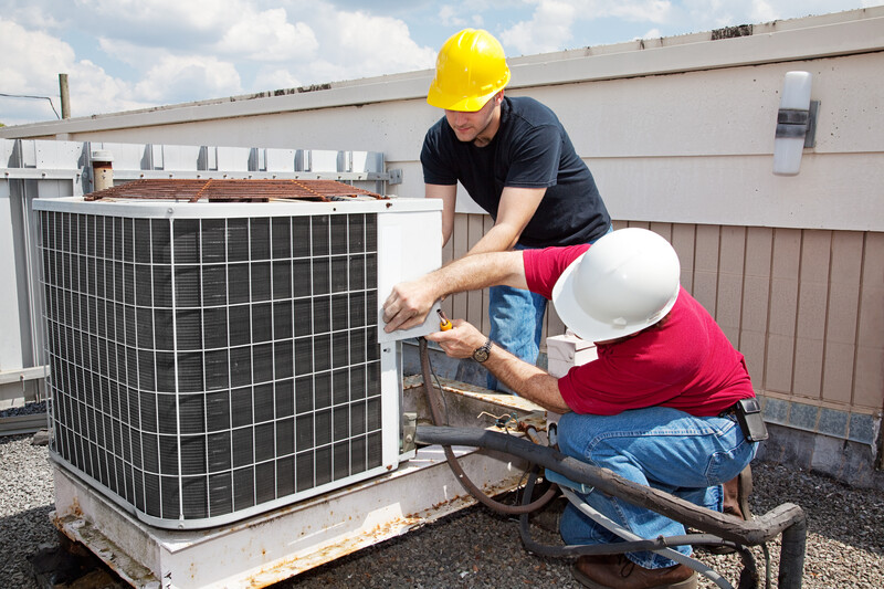 Two workers on the roof of a building working on the air conditioning unit.