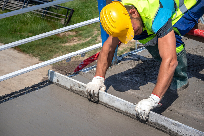 Worker with yellow helmet straighten and smoothing fresh concrete on a construction site