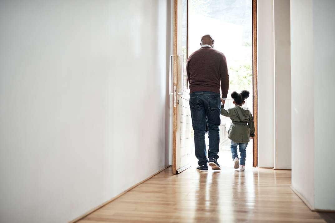 Adult man and little girl leave house through open doorway holding hands with their backs to us