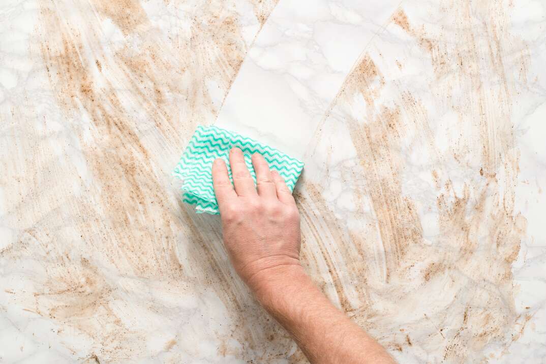 Hand Wiping Clean a Dirty Marble Surface with Paper Towel