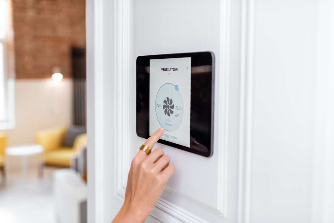 A closeup of a female hand with a gold ring on the index finger operates a modern looking touchscreen on the white wall of a home that displays the controls of a smart ventilation system, white wall, female, female hand, gold ring, index finger, touchscreen, digital display, digital, smart ventilation system, smart technology, smart tech, technology, tech, ventilation system, ventilation, HVAC