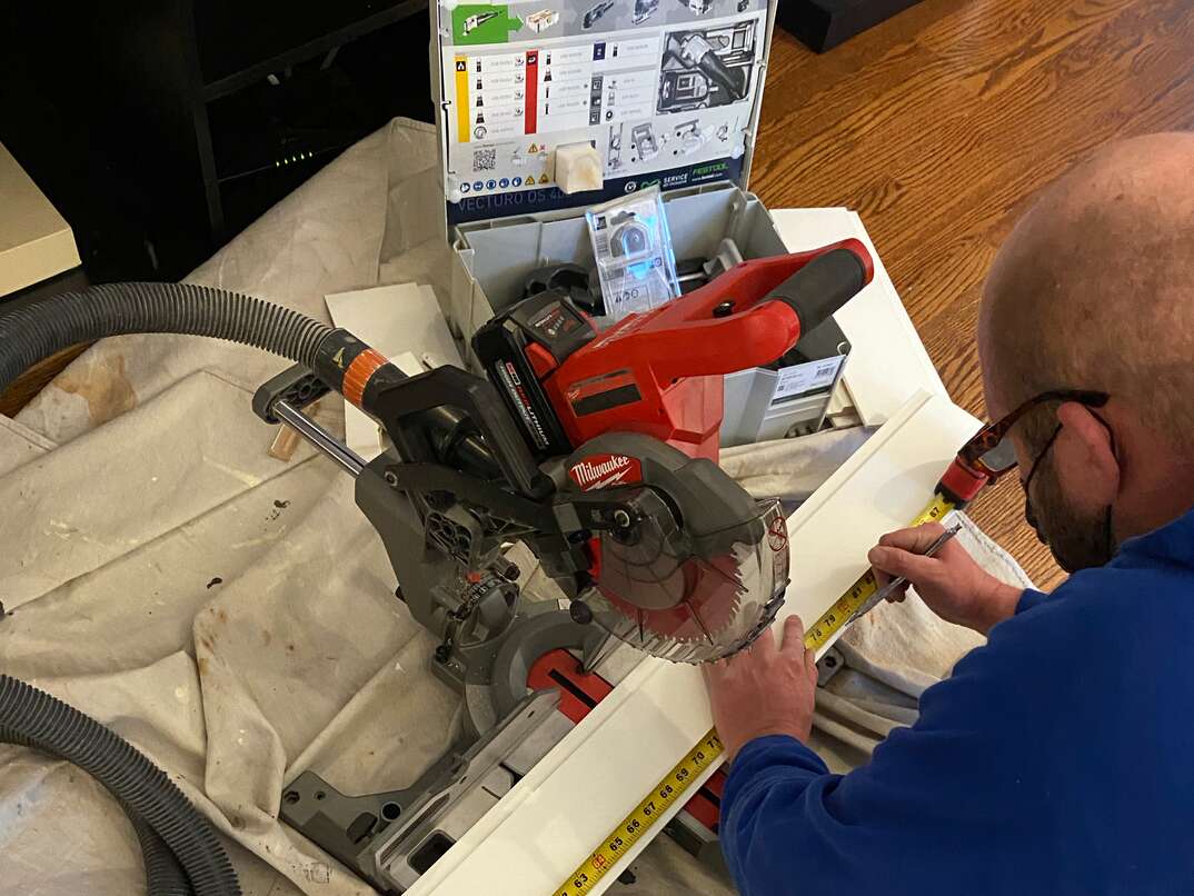 worker uses a battery-powered Milwaukee miter saw to make cuts on primed shiplap boards