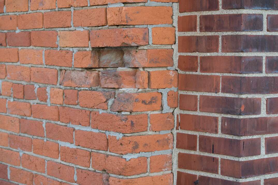 The corner of a red brick wall with the left side in disrepair and the right side in good condition