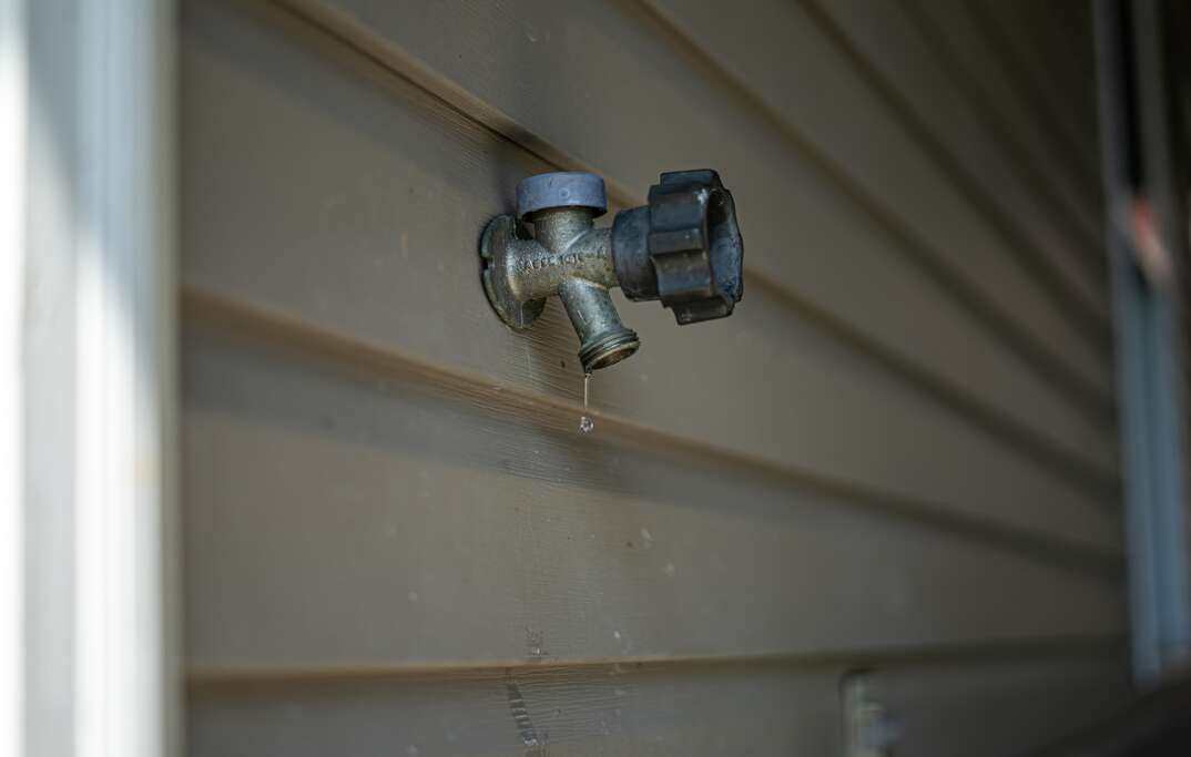 Angled shot of an outdoor faucet frozen dripping water  The crystal clear drops of water dramatically stand out from the vinyl wall and shine 