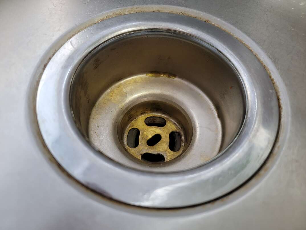 Closeup overview of stainless steel sink drain shows where the circular sink flange inserts into the sink basin.