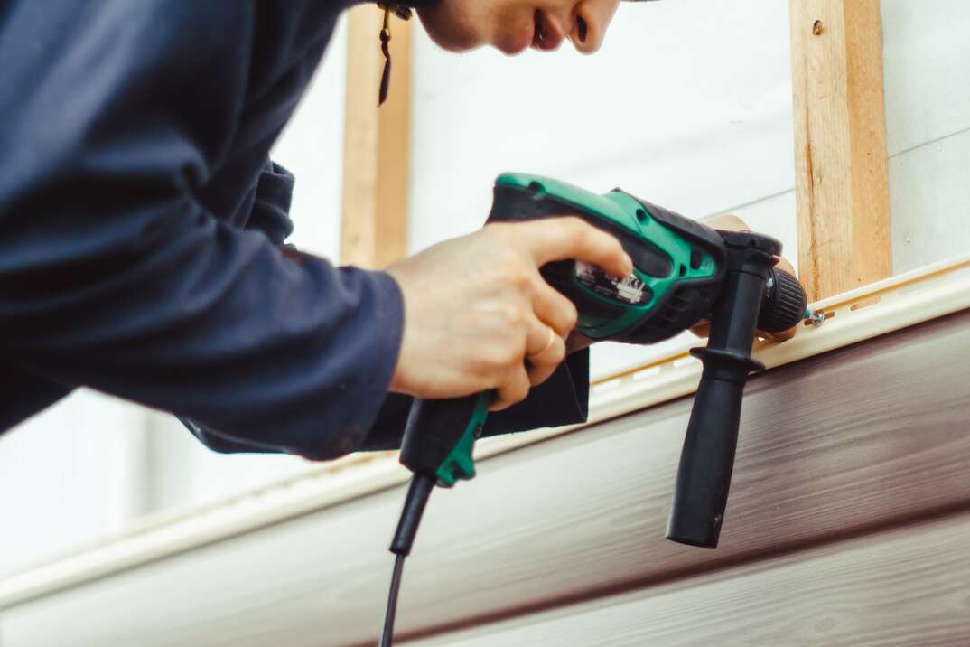 contractor is installing vinyl siding using a power drill