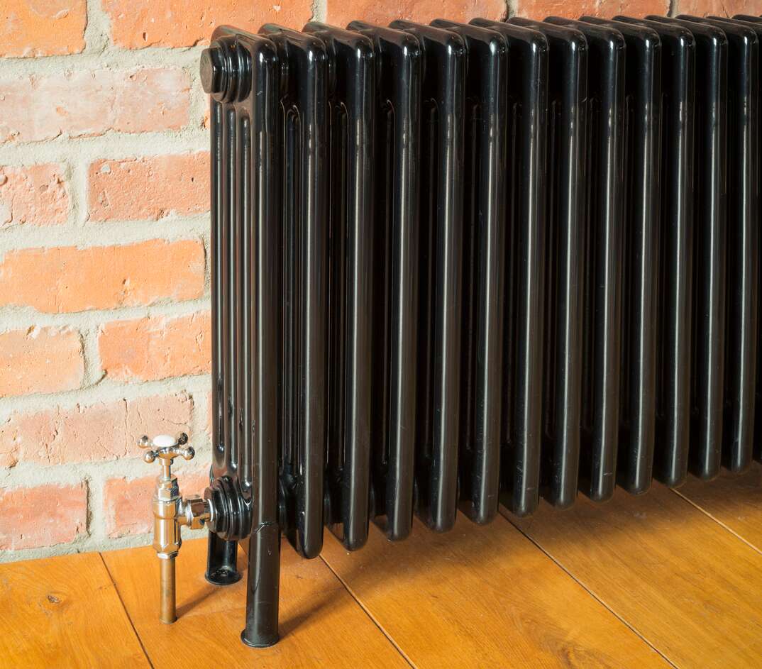 Detail of an old fashioned   retro radiator against a brick wall 