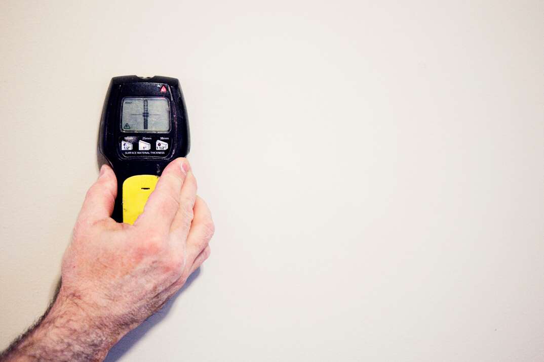 Stud Finder being held by a man against a painted drywall