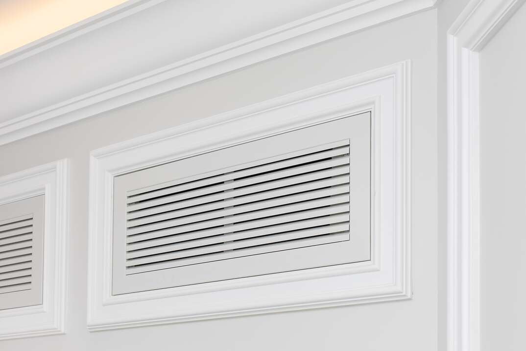 Ventilation grate of conditioning system decorated and disguised with classic white moldings in modern interior.