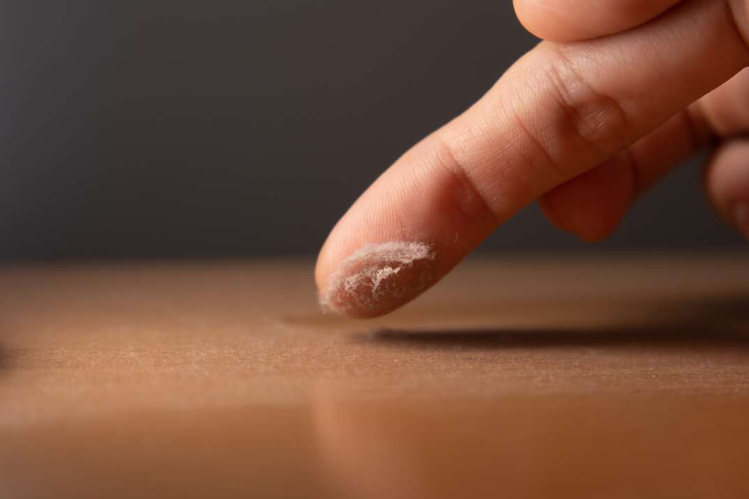 Touching the dust on a surface of furniture with finger