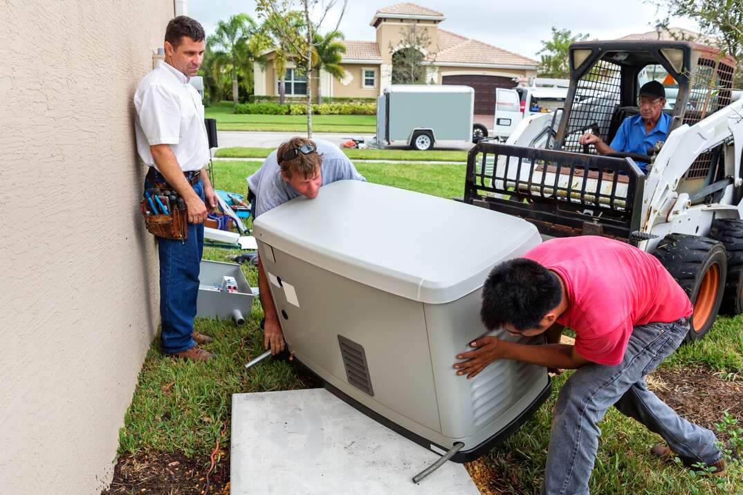 a group of male contractors and a forklift position a large home generator on to a concrete slab