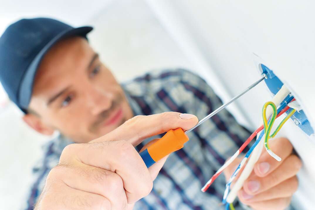 electrician fixing wall outlet with screwdriver