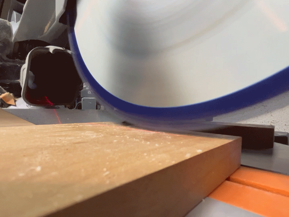 a powered miter saw lowers on a piece of alder wood at a 90 degree angle.