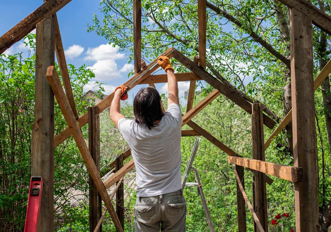 Man building wooden roof using tape measure