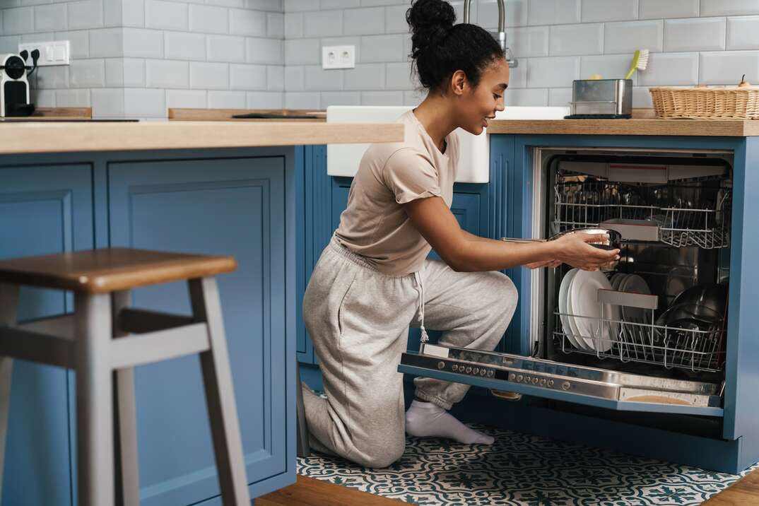 Happy black woman smiling while using dishwasher at home kitchen