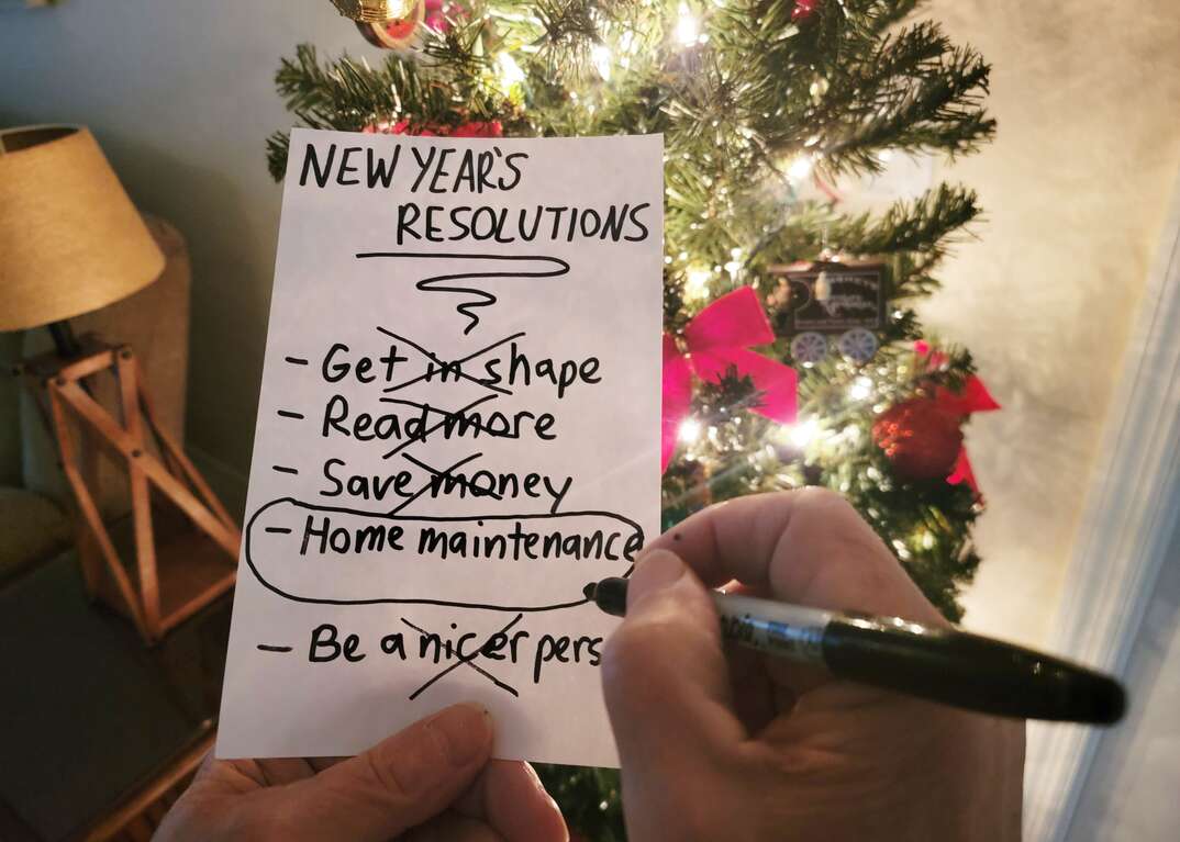 A man holds his New Year s resolutions in hand in front of the Christmas tree and circles home maintenance as the one he intends to accomplish