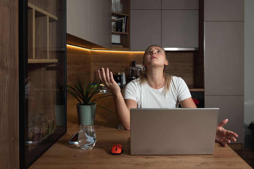 A woman sitting at a desk working on a laptop computer looks up at the ceiling with an annoyed expression due to evident noise coming from the condo or apartment above, woman, looking up, woman looking up, condo, condominium, apartment, annoyed, angry, disturbed, disturbance, noise, noisy, loud, computer, laptop computer, desk, desktop