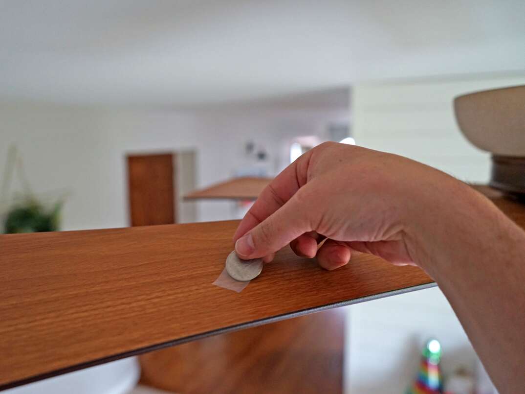 person placing a quarter on to a ceiling fan blade with a piece of scotch tape 