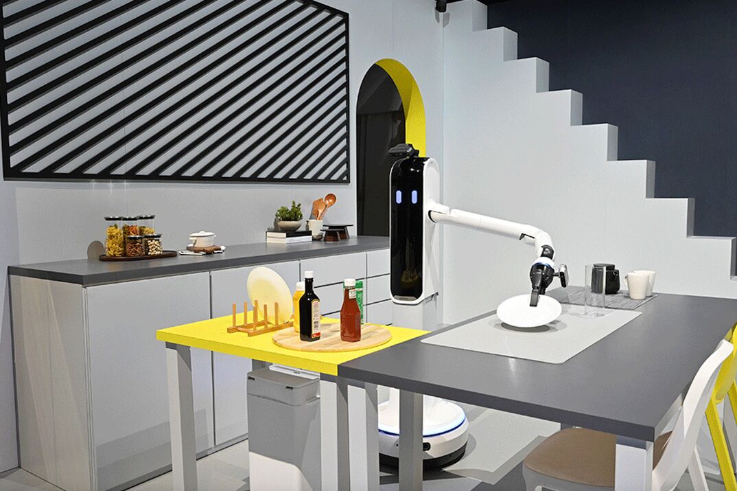 A domestic robot arm moves a plate to the table of a futuristic kitchen in this illustration