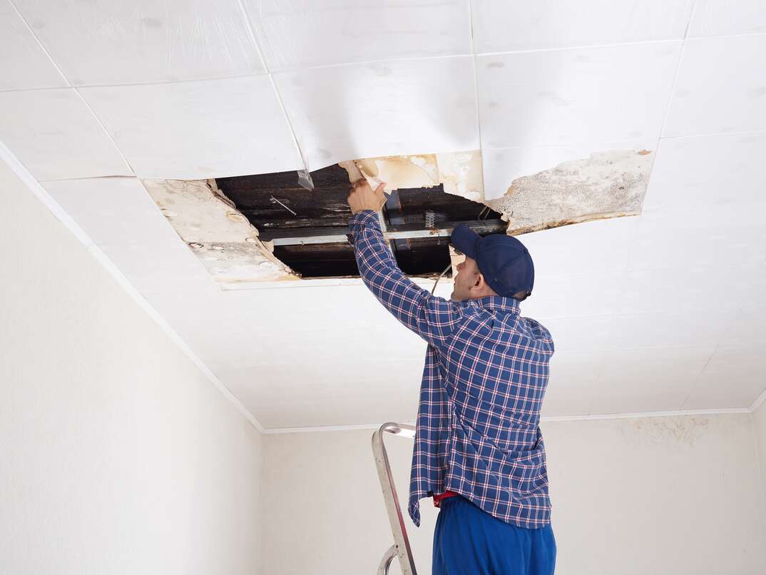 Man repairing collapsed ceiling. Ceiling panels damaged  huge hole in roof from rainwater leakage.Water damaged ceiling .