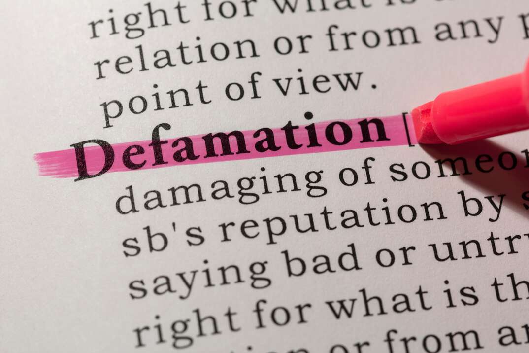 A closeup image of a pink highlighter draws a pink line across the word defamation on a page of a dictionary, defamation, defamation of character, slander, libel, tort law, legal, law, lawsuit, attorney, attorney at law, civil case, civil suit, highlighter, pink highlighter, dictionary, book, page, definition, define, define terms