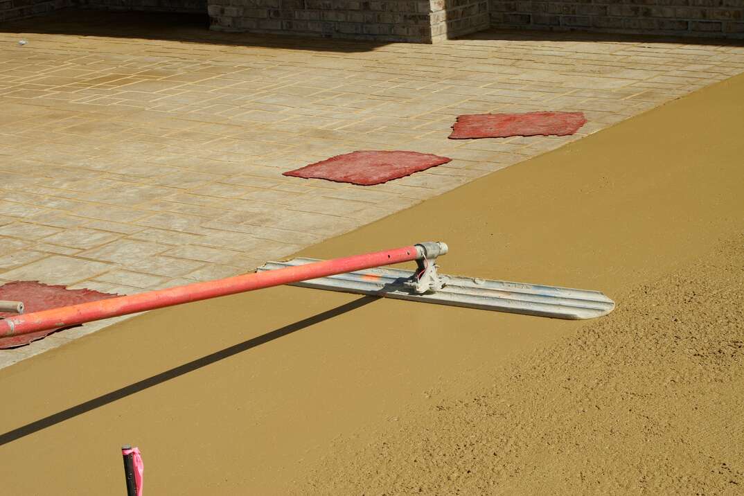 A concrete driveway gets prepped for stamping with rubber  brick  stamps laying nearby 