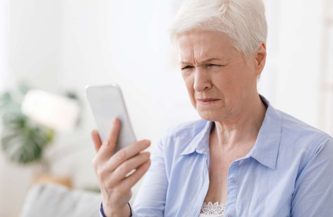 Myopia Concept. Elderly woman squinting while looking at smartphone screen, trying to read message, closeup