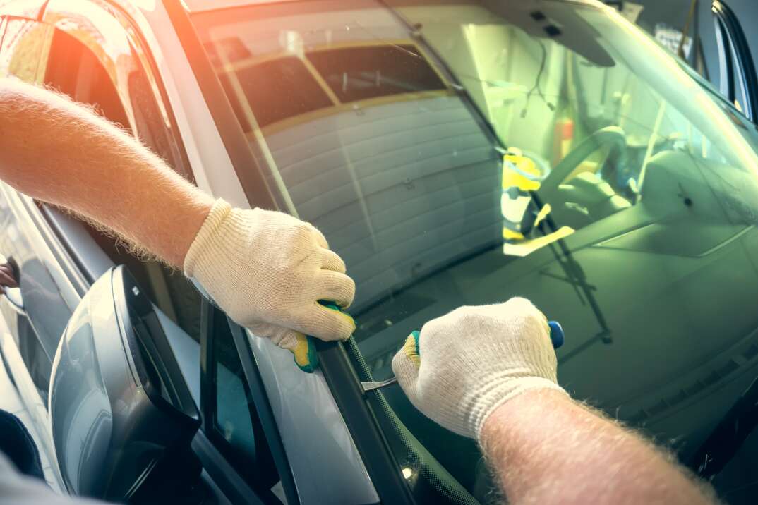 Service worker dismantle broken glass windscreen or windshield before installing new one on car in auto station garage.