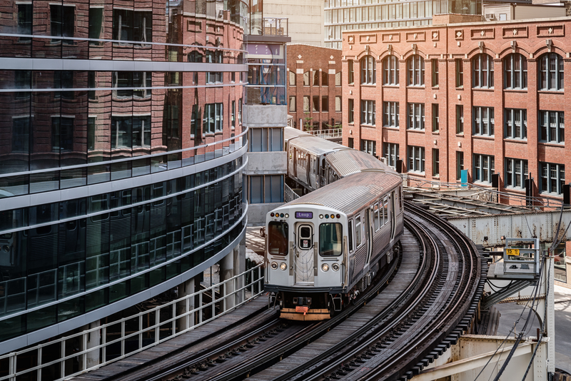 A Chicago elevated train goes around a bend in the train tracks with large buildings on either side of it, train, elevated train, subway, public transportation, transportation, bend in train tracks, tracks, buildings, large buildings, tall buildings, urban skyline, urban canyon, skyline, brick buildings
