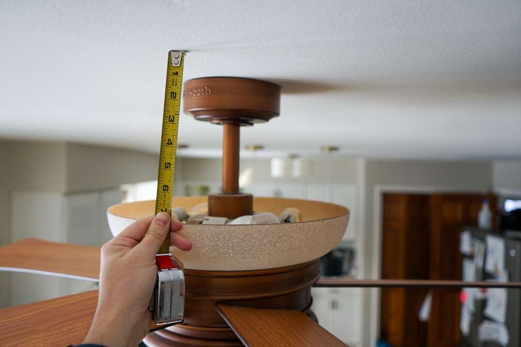 man hold a tape measure alongside a ceiling fan s downrod 