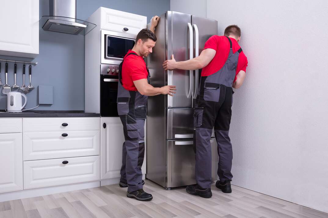 Two Young Male Movers Placing a stainless Steel Refrigerator In Kitchen remodel