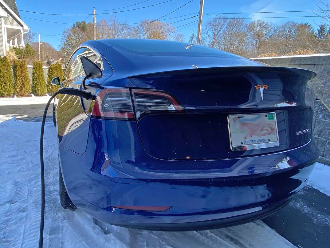Blue 2018 Tesla Model 3 in a residential driveway getting charged 