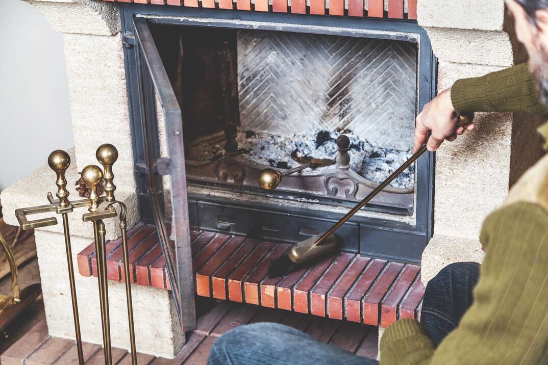 man cleans the furnace of fire with a spatula and brush on a long handle