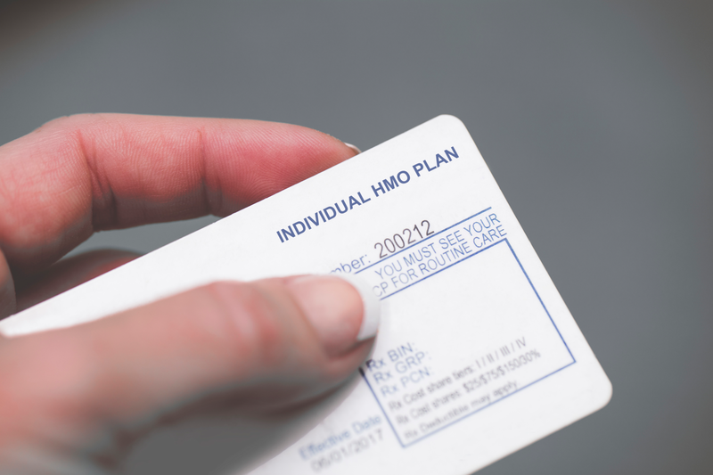 A human hand holds a medical insurance card showing that the holder has an HMO health coverage plan, medical insurance, medical, health insurance, health, insurance, coverage, HMO, health maintenance organization, HMO, PPO, medical card, medical, card, human hand, human, hand, insurance plan, plan