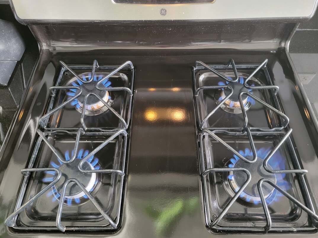 A black gas range stovetop has all four burners on emitting blue flames under black metal stove grates.