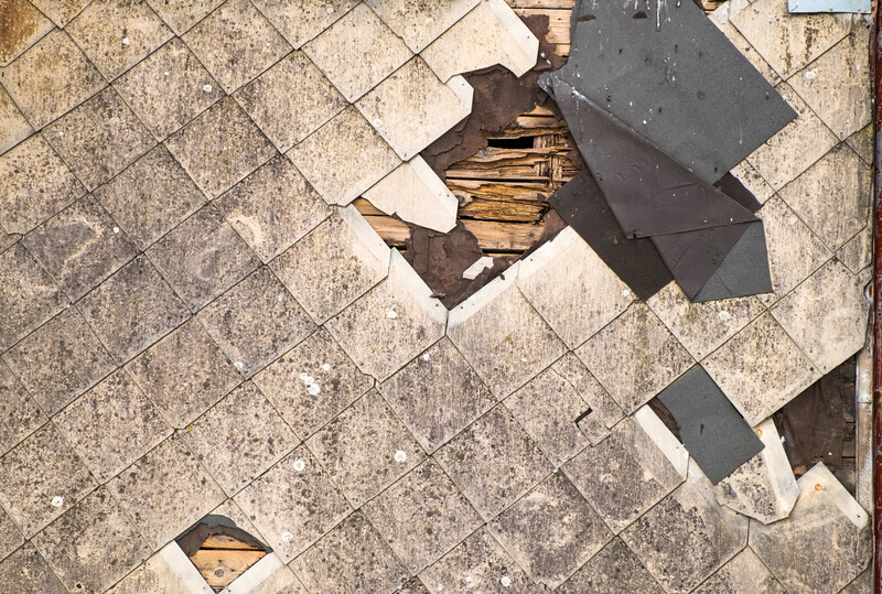 Old damaged roof of asbestos shingles requiring repair. Dirty beams and torn waterproofing of roofing material.