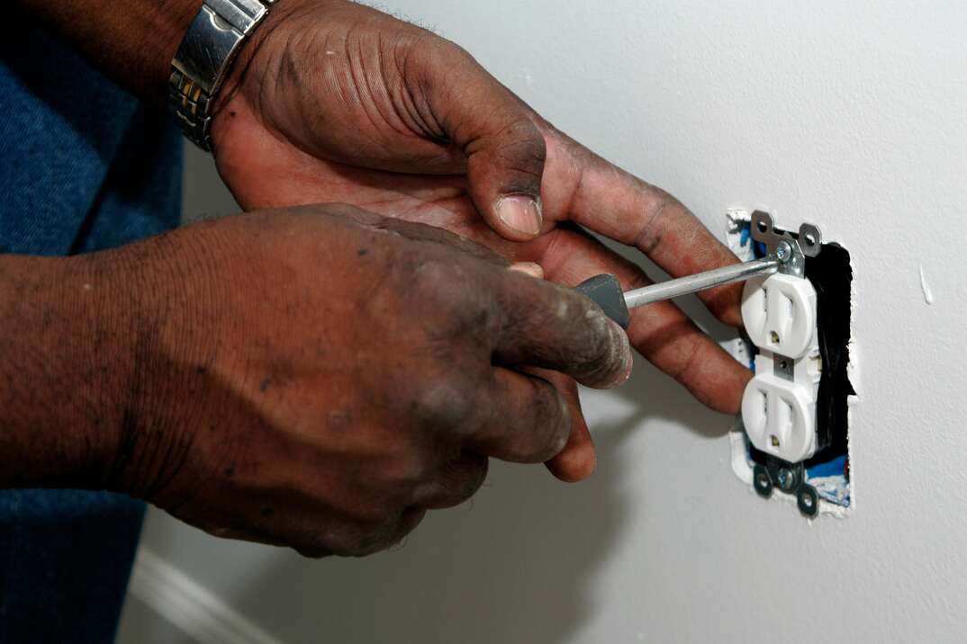 A pair of Black hands using a scewdriver to install an electrical outlet