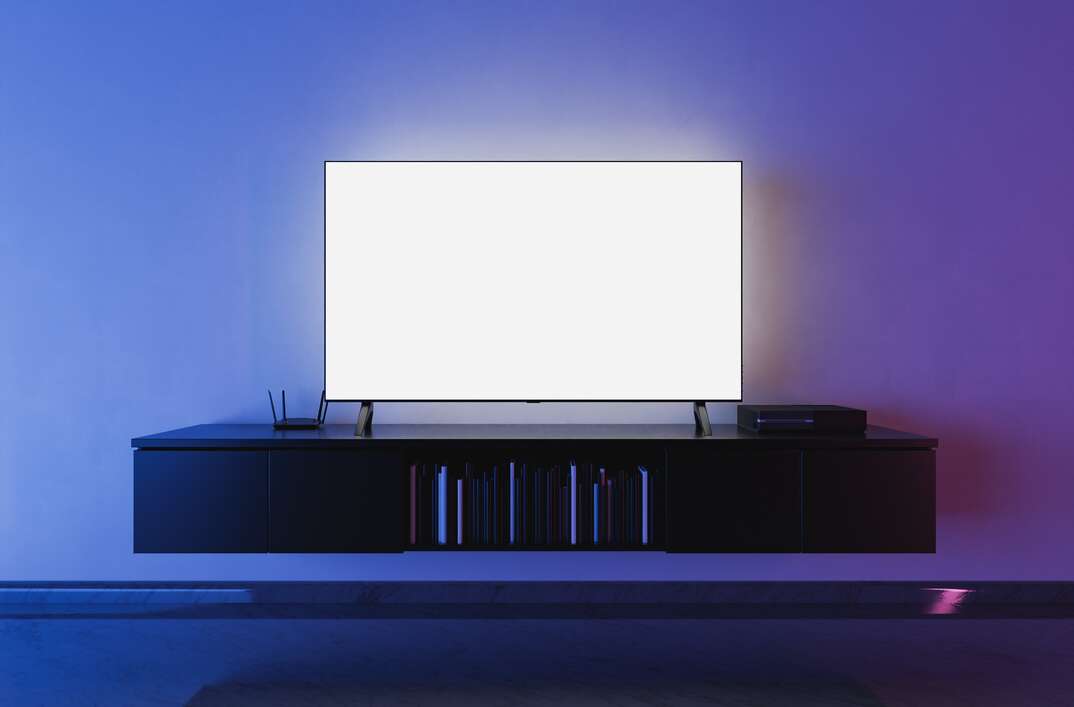 A flatscreen TV with a glowing display sits atop a mounted floating entertainment center in a dark living room