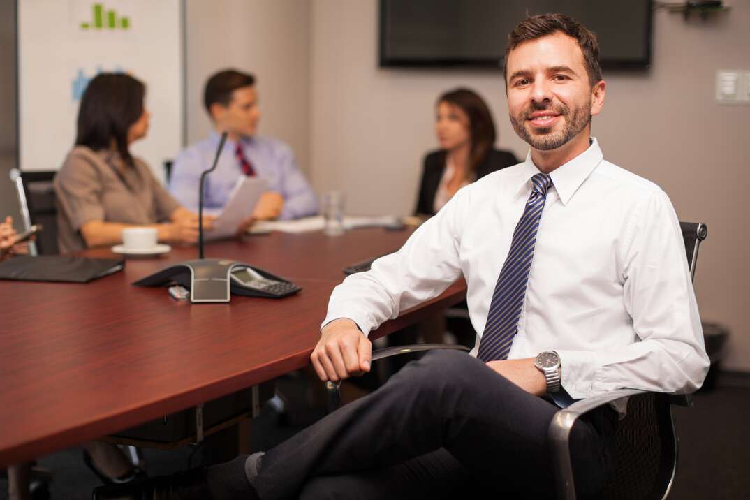 Handsome young lawyer wearing a tie sitting with some of his co-workers in a meeting room and smiling