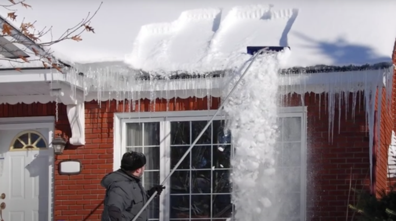 man raking snow from roof