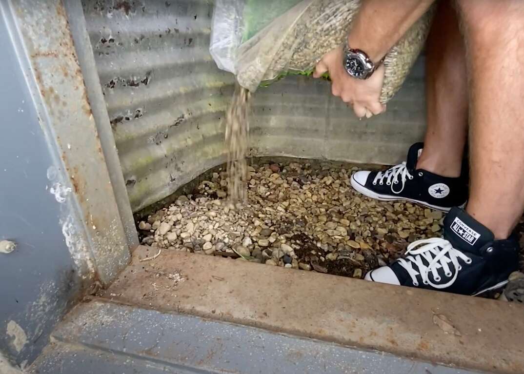 Landscaping gravel sits at the base of a corrugated steel window well of a basement egress window