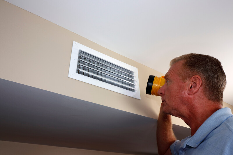 A man shines a flashlight into an HVAC return vent to investigate a problem, HVAC, heating ventilation and air conditioning, air conditioning, AC, AC return, return, vent, AC vent, HVAC vent, air conditioning vent, heat vent, blower, flashlight, outage, man, homeowner, shining flashlight, climate control, duct, HVAC duct, AC duct, air duct