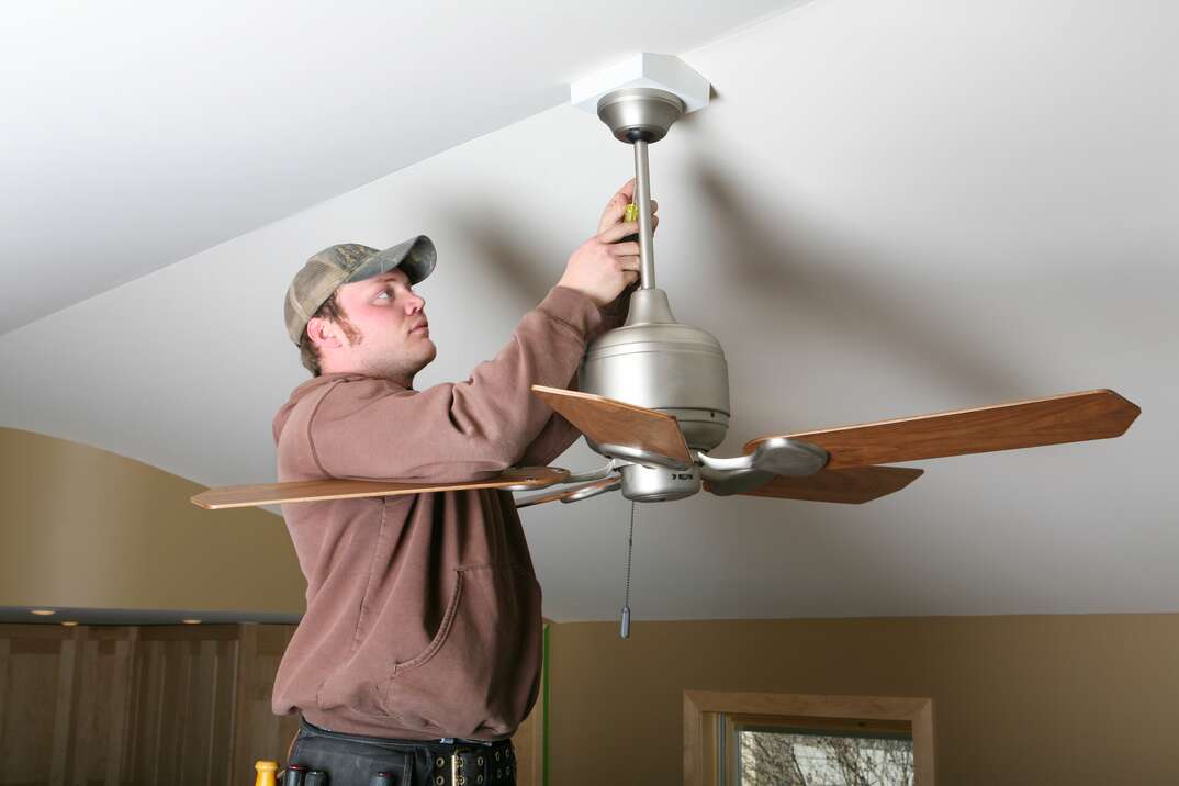 an electrician works to install a ceiling fan with a downrod 