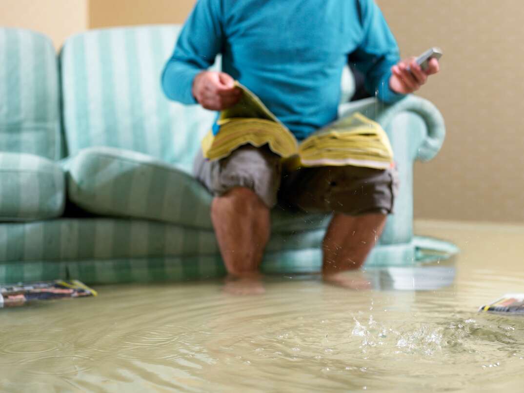 Man sitting in flooded living room using phone