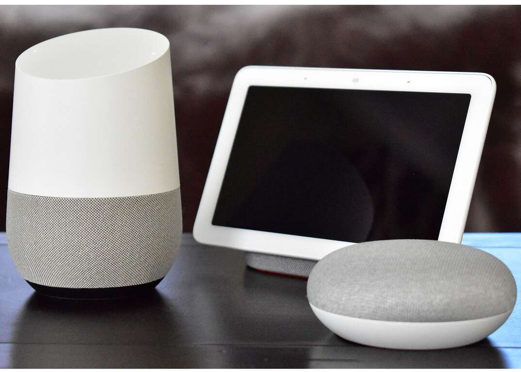 A Google Nest Hub device sits next to compatible smart speakers on a table.