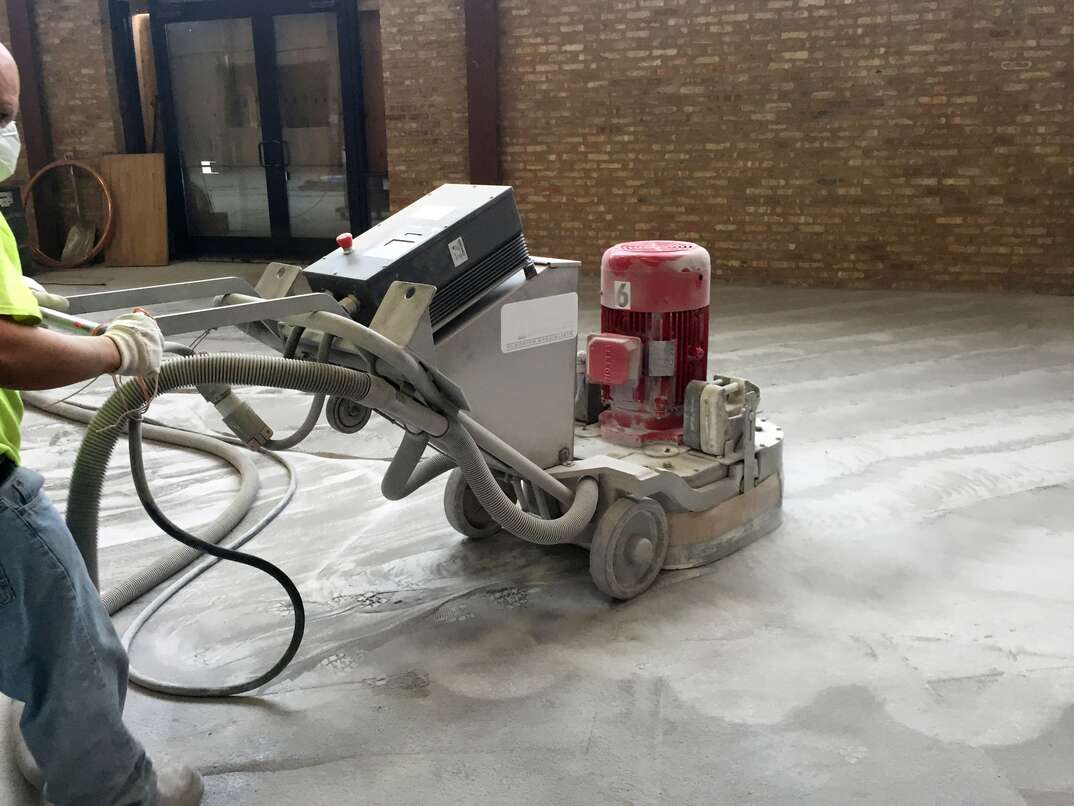 A contractor weilds a large floor grinding  polishing machine to sand down a new Terrazo floor