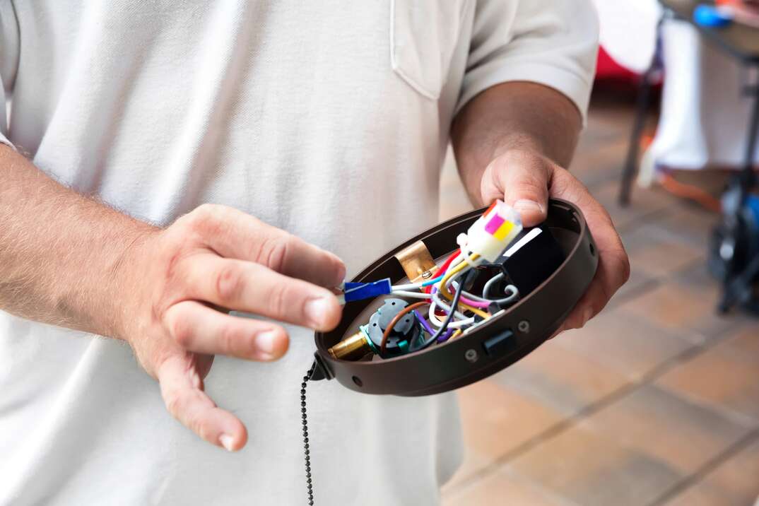 close up of an electrician holding the upper shroud of a residential ceiling fan to display the wiring 